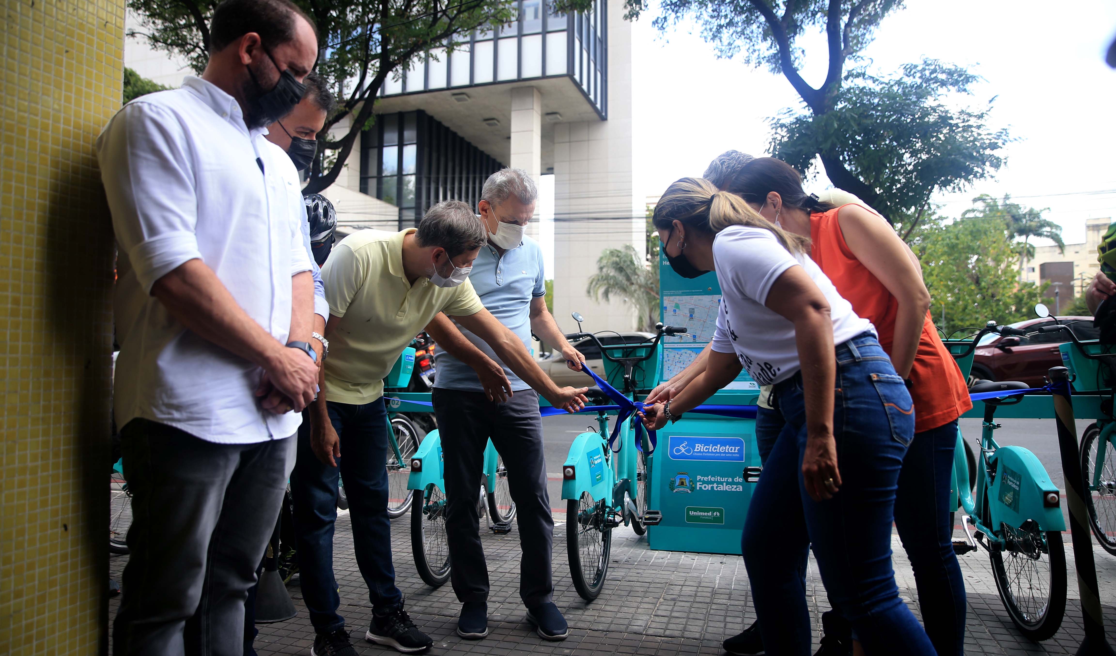 grupo de pessoas na frente de uma estação do bicicletar, onde ficam estacionadas as bicicletas